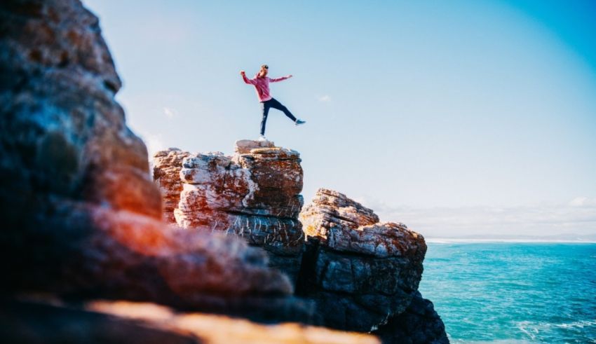 A woman jumping off a cliff in front of the ocean.