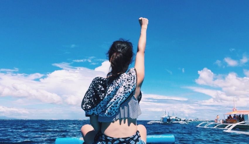 A woman is riding a boat in the ocean with her arms raised.