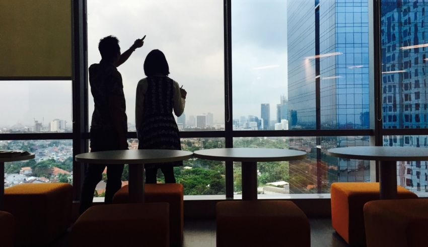 Two people standing in front of a window with a view of a city.