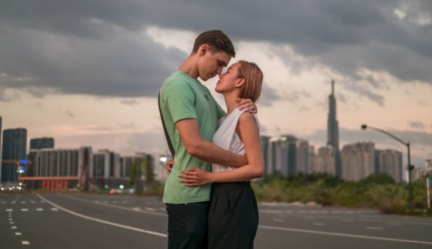 A young couple embracing in the middle of an empty road with a city skyline in the background.