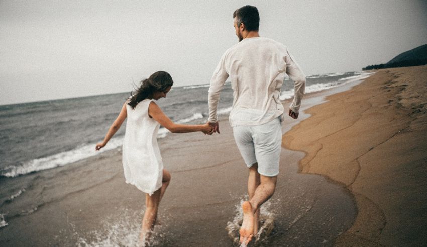 A man and woman running on the beach with their hands in the water.