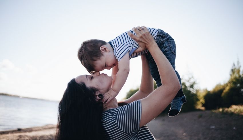 A woman is holding her son up in the air at the beach.