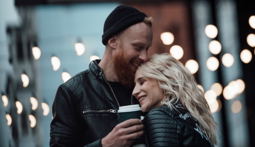 A man and a woman holding a cup of coffee in front of lights.