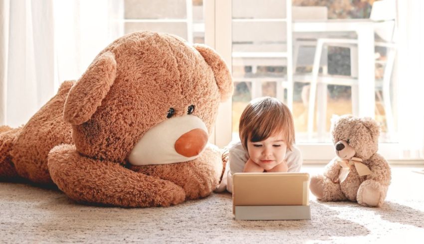 A child is laying on the floor next to two teddy bears.