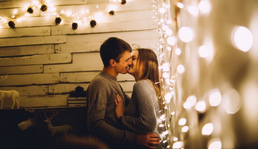 Couple kissing in front of christmas lights.