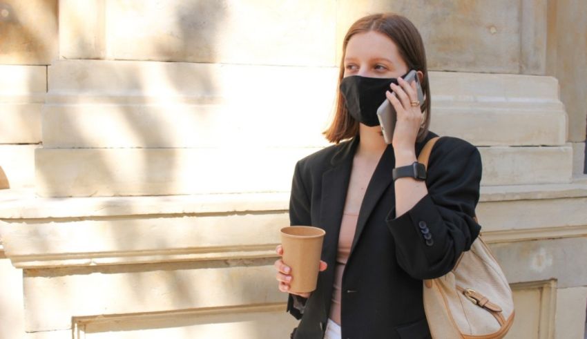 A woman wearing a face mask and holding a cup of coffee.