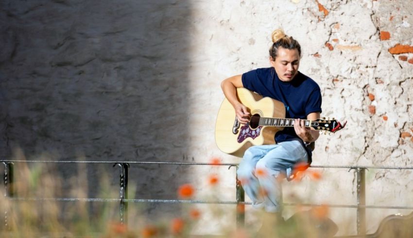 A young woman playing an acoustic guitar in front of a wall.