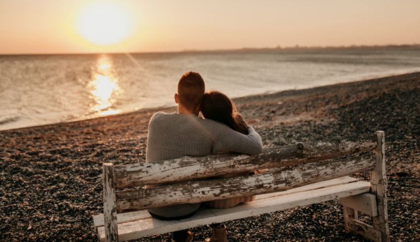 A couple sitting on a bench at sunset.