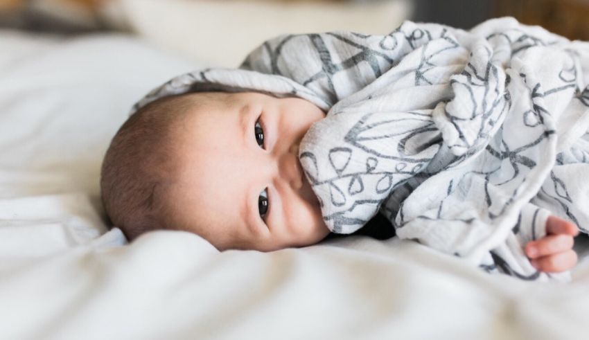 A baby laying on a bed with a swaddle blanket.