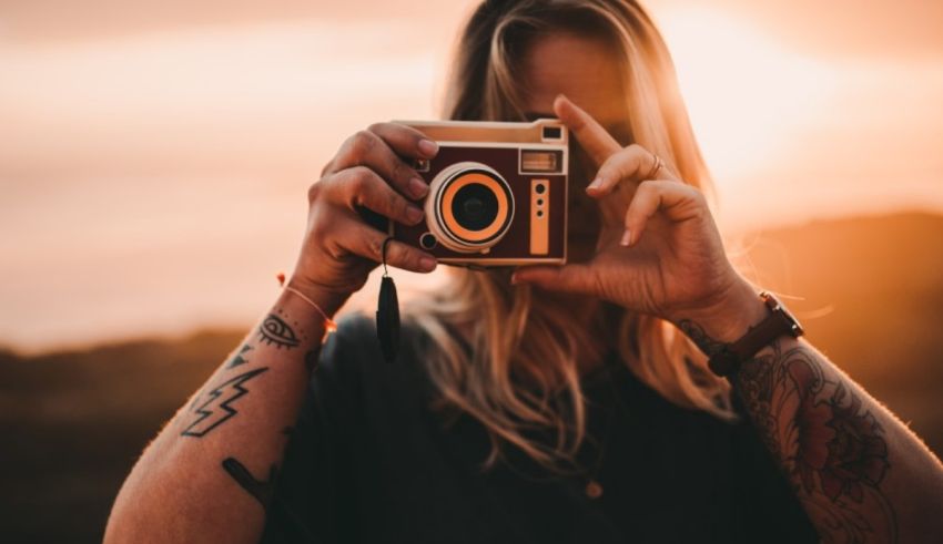 A woman with tattoos taking a photo with an old camera.