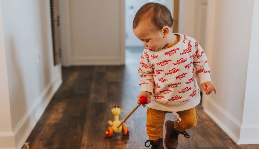 A toddler playing with a wooden toy on a wooden floor.