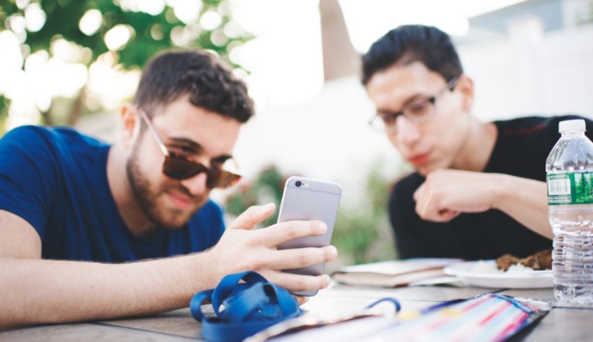 Two young men sitting at a table looking at their phones.