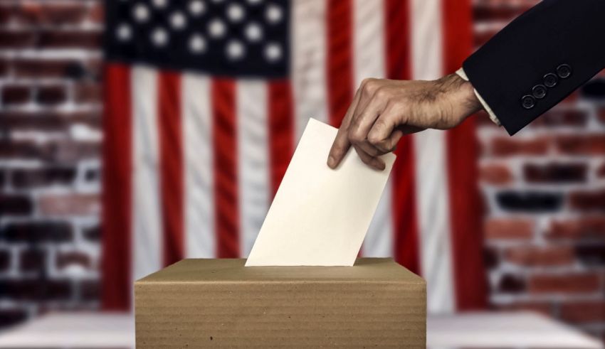 A hand putting a paper into a voting box in front of an american flag.