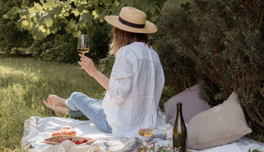 A woman is sitting on a blanket in the grass with a glass of wine.