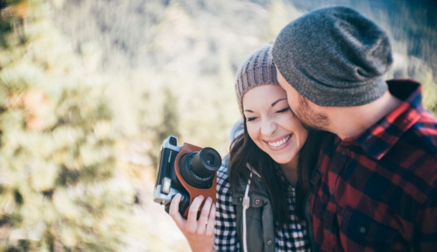 A couple kissing while holding a camera in the mountains.