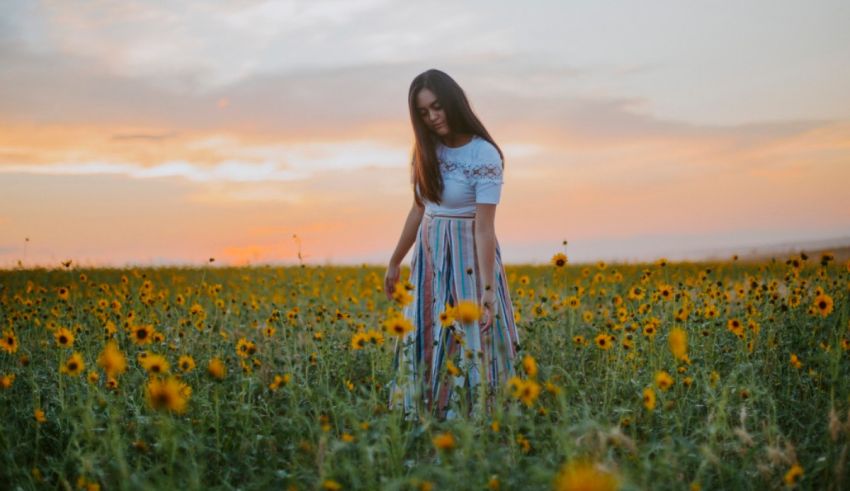 A girl standing in a field of sunflowers at sunset.