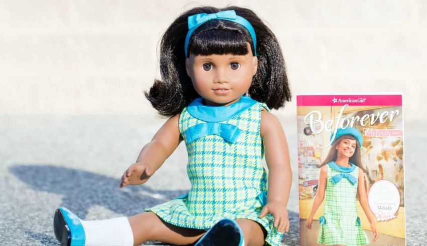 A doll is sitting on the ground next to a book.