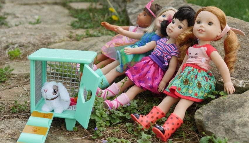 A group of dolls are sitting on the ground next to a rabbit cage.