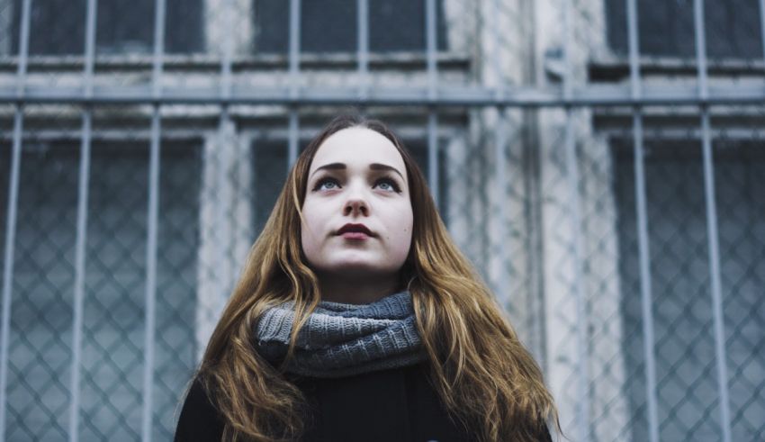 A young woman with long hair standing in front of a fence.