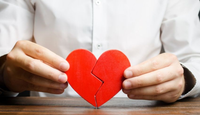 A man holding a broken red heart in his hands.