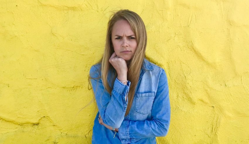 A young woman leaning against a yellow wall.