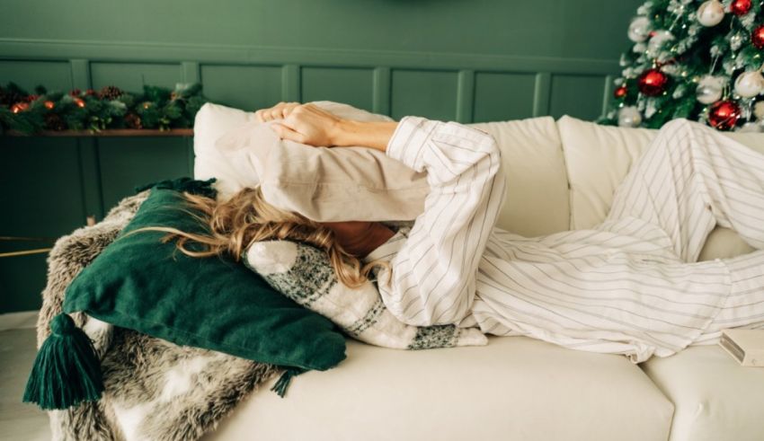 A woman in pajamas laying on a couch in front of a christmas tree.