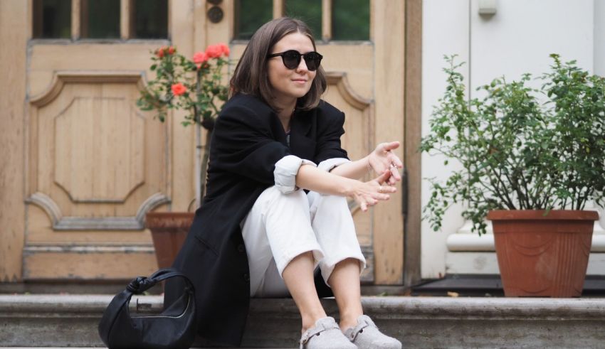 A woman sitting on the steps wearing sunglasses and a blazer.