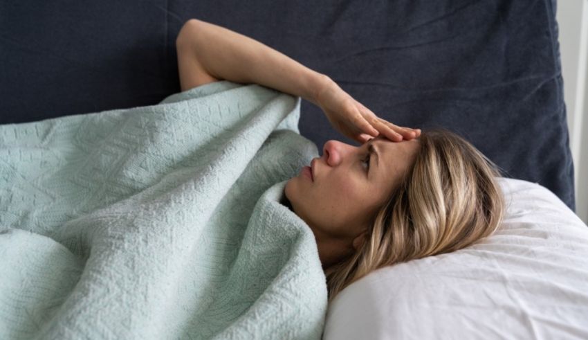 A woman lying in bed with her hand on her forehead.