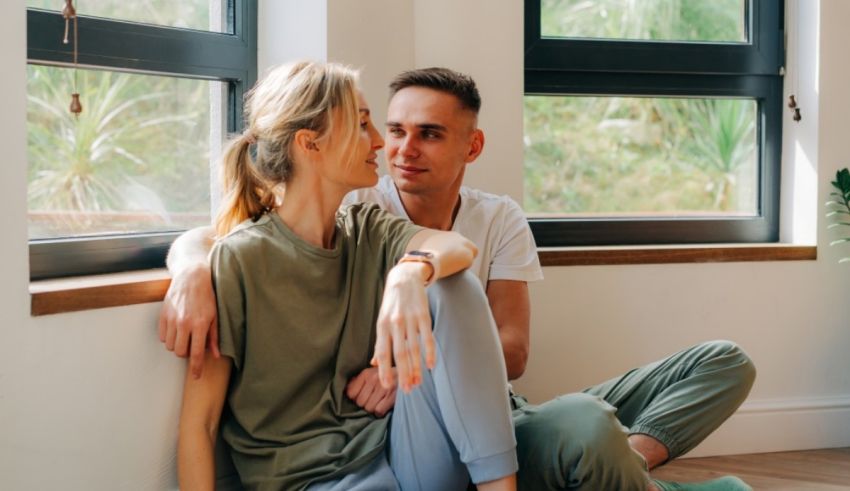 A couple sitting on the floor in front of a window.