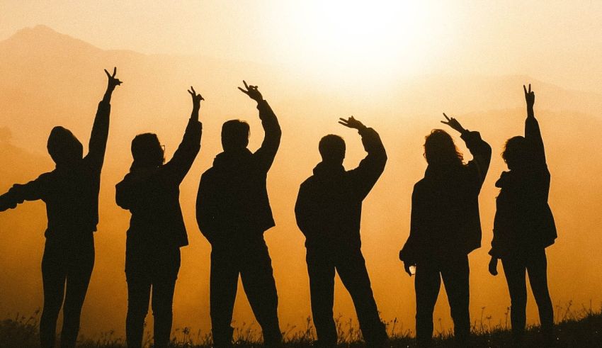 A group of people raising their hands in the air at sunset.