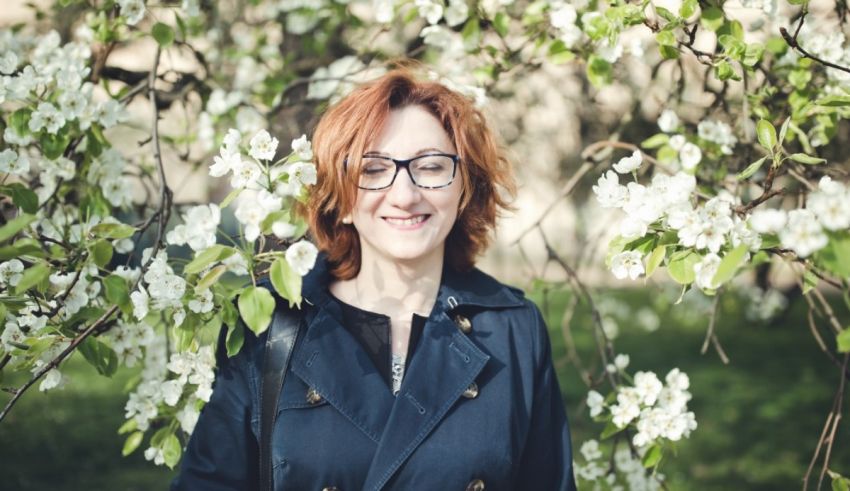 A woman in glasses smiling in front of a blossoming tree.