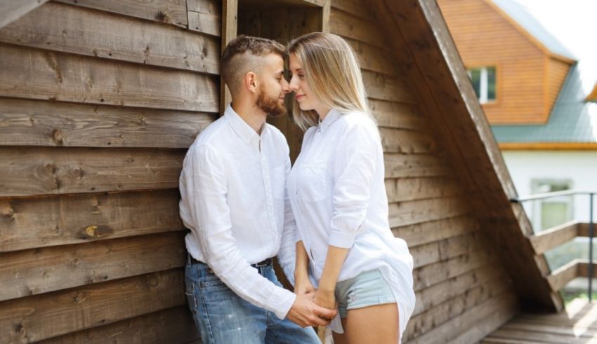 Young couple hugging in front of a wooden house.