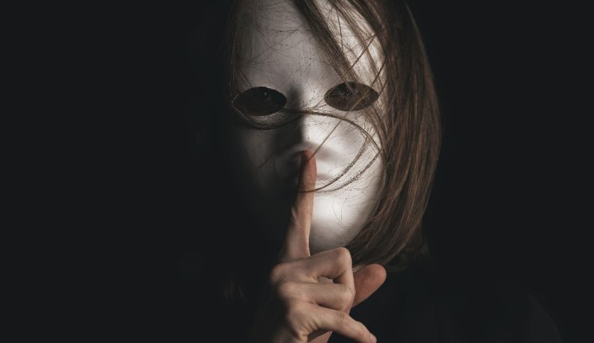 A woman wearing a white mask with a finger on her lips.