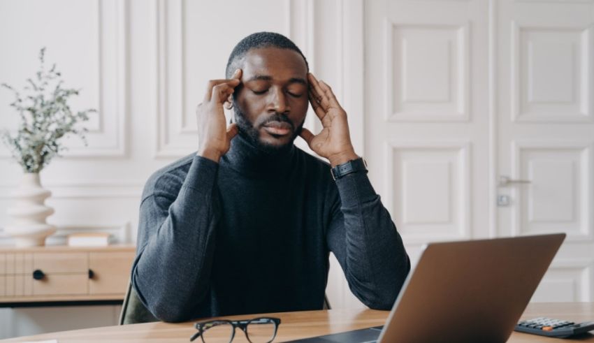 A man sitting at a desk with his hands on his temples.