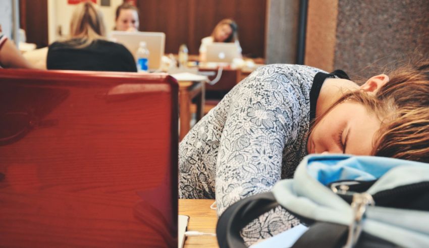 A woman is sleeping at a table with laptops.