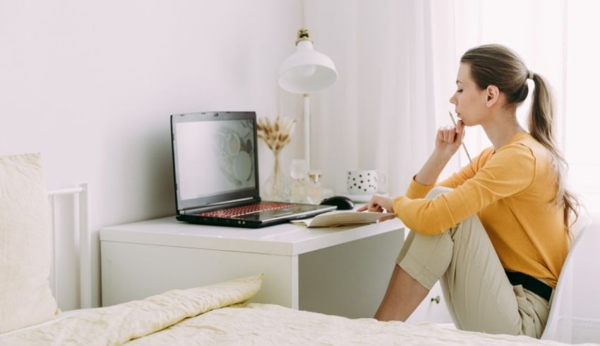 A woman sitting on a bed with a laptop in front of her.