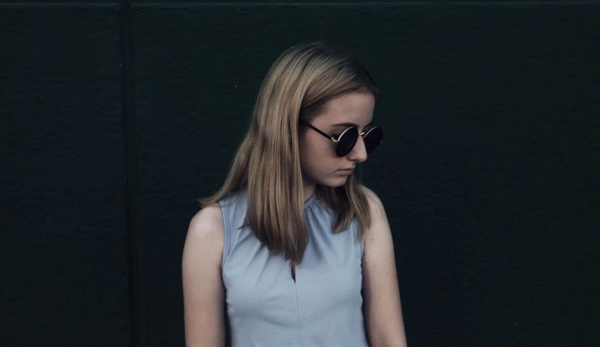 A girl wearing sunglasses leaning against a wall.