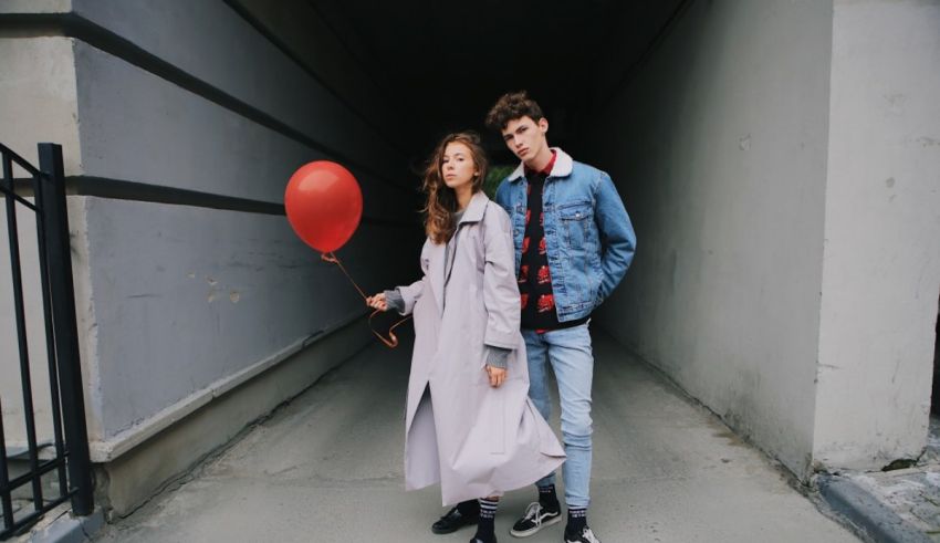 A young couple holding a red balloon in an alleyway.