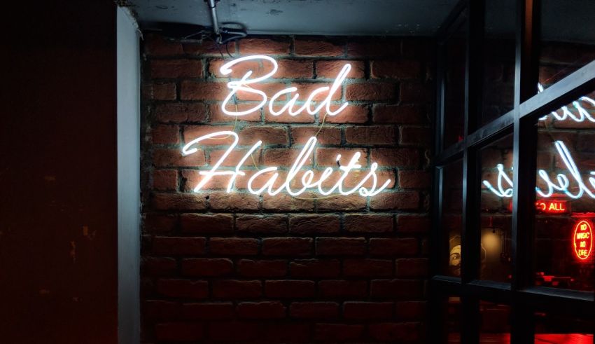 A neon sign that says bad habits in front of a brick wall.