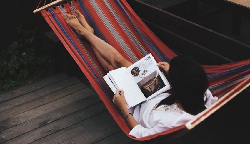 A woman laying in a hammock reading a book.
