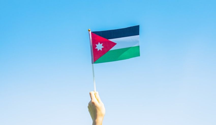 A hand holding a jordan flag against a blue sky.