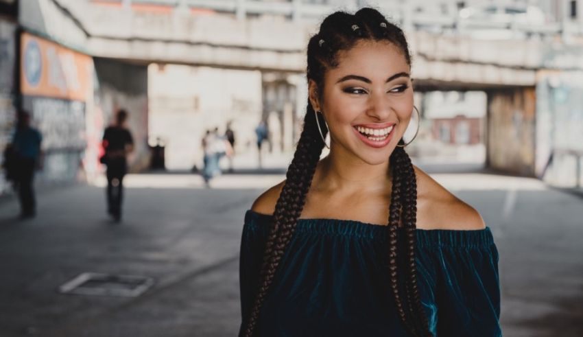 A woman with braids smiling in an alleyway.