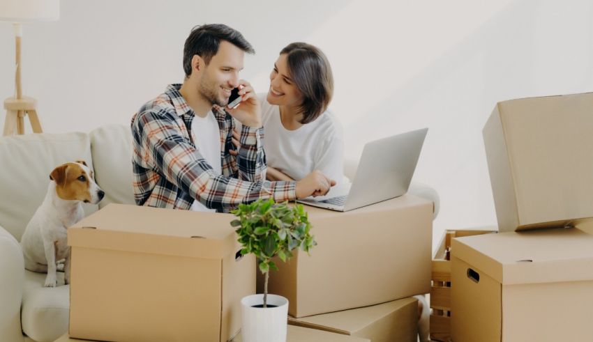 A man and woman sitting on a couch with boxes and a dog.