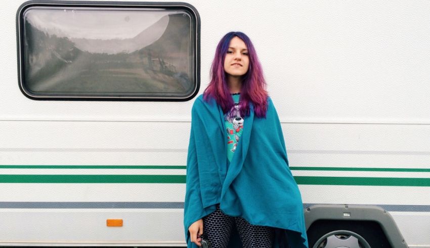 A young woman with purple hair standing in front of a rv.