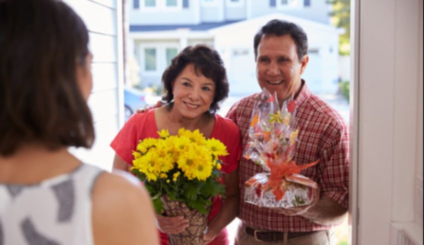 A man and woman giving flowers to each other in front of a house.