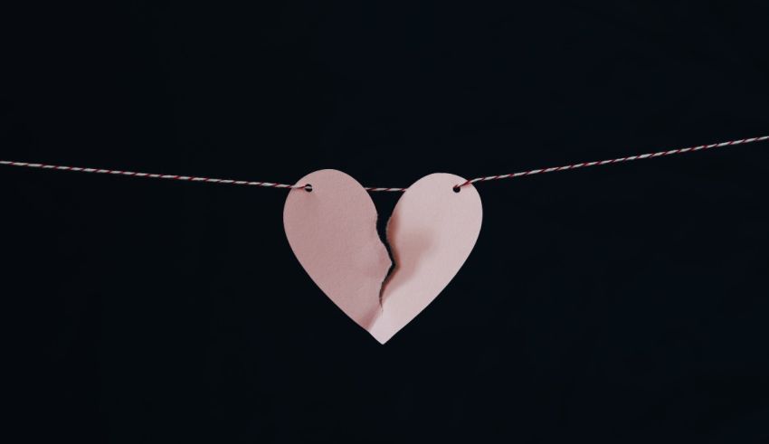 A broken heart hanging from a string on a black background.