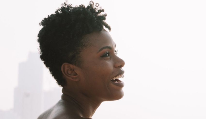 A black woman with afro hair is smiling in front of a city.