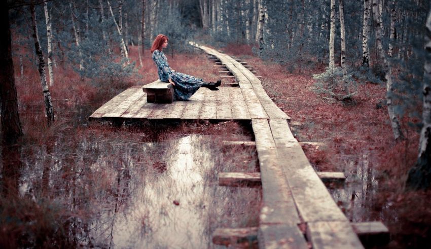 A woman sitting on a wooden bridge in the woods.