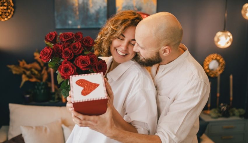 A man and woman hugging while holding a box of roses.