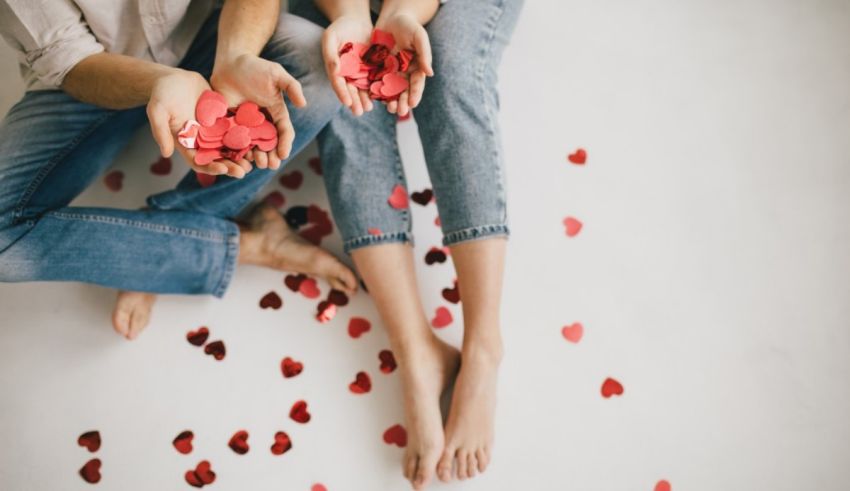 Valentine's day couple sitting on the floor with red hearts in their hands.